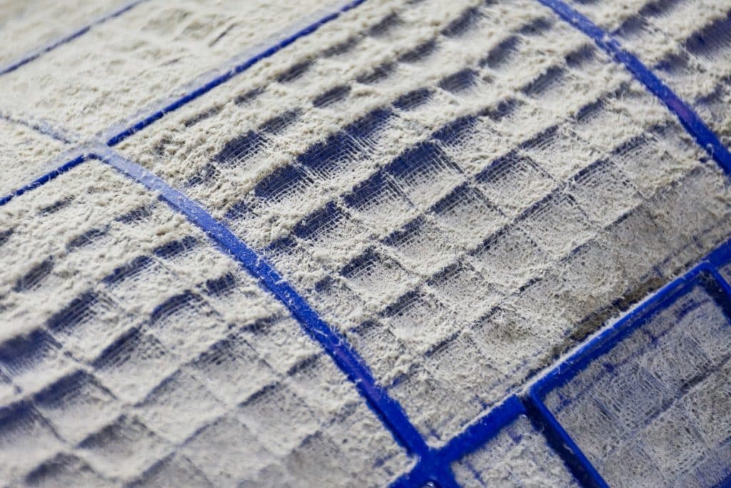 A close-up of a heavily dust-covered air conditioner filter, with thick white lint and debris clogging the blue mesh grid.