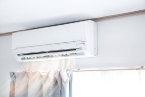 Wall-mounted split air conditioner blowing cool air above a window with curtains.